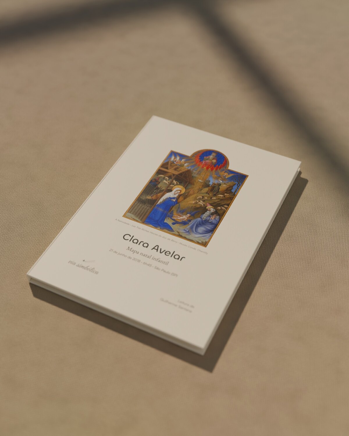 O Mapa Natal Infantil impresso como livro, com a Natividade na capa, sobre uma toalha de linho, na luz de uma janela